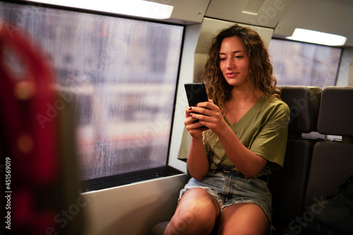 Young beautiful girl tourist travels by train. Happy smiling woman using the phone while travel by train