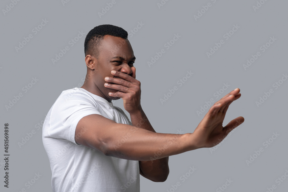 A dark-skinned man in a white thsirt closing his nise A dark-skinned man in a white thsirt closing his nise
