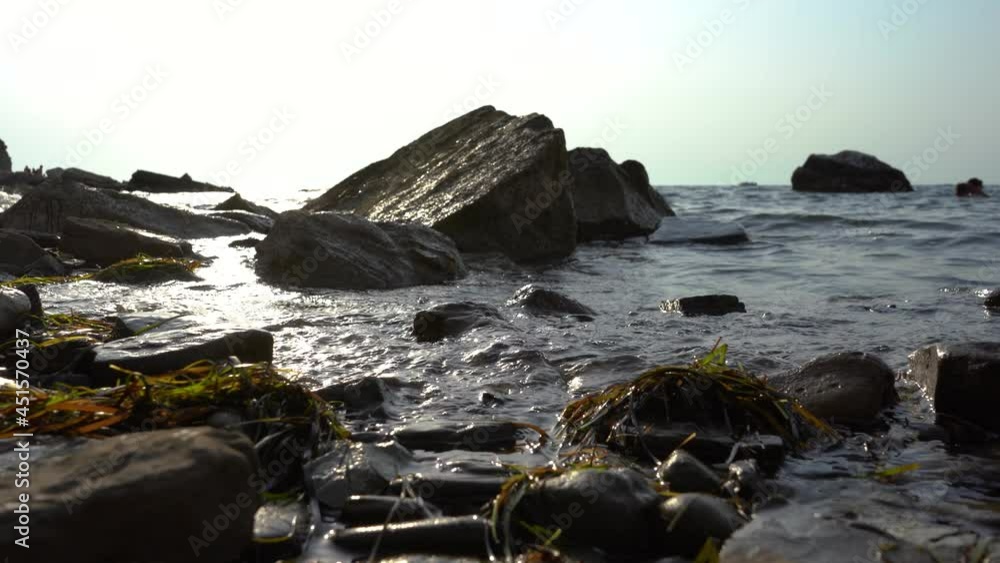 Low angle view of calm waves hitting rocky shore. Bright sunny day. Adriatic shore. Close up view of rocky shoreline and flooded seagrass. Static shot, shallow depth of field Low angle view of calm waves hitting rocky shore. Bright sunny day. Adriatic shore. Close up view of rocky shoreline and flooded seagrass. Static shot, shallow depth of field