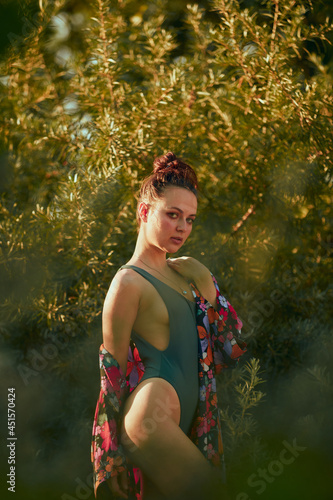 Seductive slender woman posing on the green leaf beach , in a sexy swimsuit and colored beach robe, tanned body, magnificent figure. Healthy nature, sun on holiday © oleg_ermak