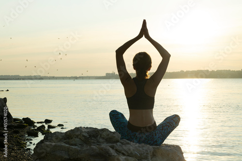 Woman sitting on the rock and doing yoga pose against sunrise,river, beautiful landscape