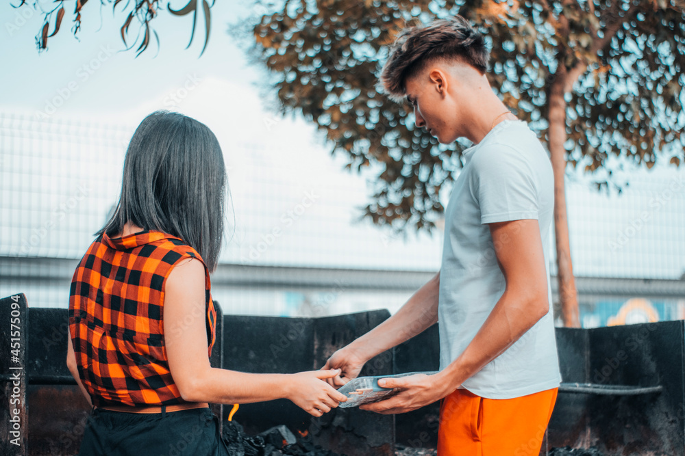 Pareja de muchachos jóvenes cocinando una barbacoa al aire libre junto a los arboles 