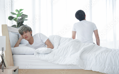 Lgbt Asian gay couple quarreling and irritated in bedroom. Young man made sullen face and lay in bed and stressed boyfriend sitting at end of bed. Homosexual in problem relationship