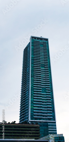 Central Jakarta, Indonesia - March 21th, 2021: A tall green building under a clear sky with fluffy clouds.