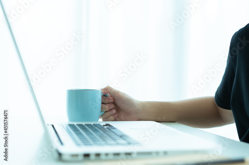 Asian young businessman in relax casual sip a hot coffee in a cup while working in the morning.