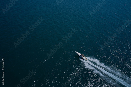 Large boat on the water in motion top view. Luxury motor boat on dark blue water aerial view. Speedboat is fast moving in dark water. Travel on high-speed boats on the water.