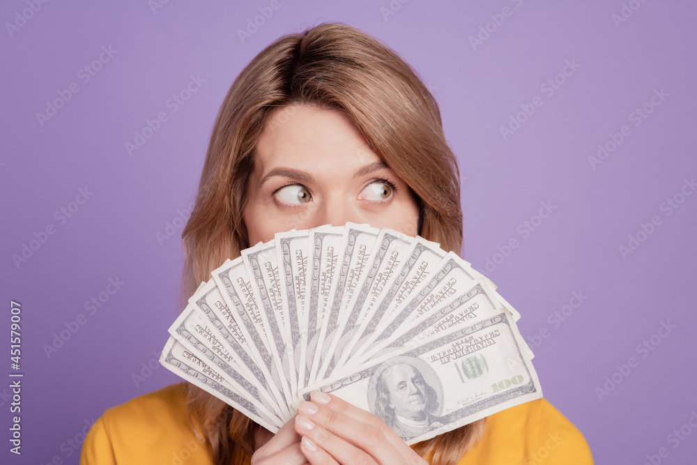 Photo of young pretty woman closing face bunch of dollars rich look empty space isolated over violet color background Photo of young pretty woman closing face bunch of dollars rich look empty space isolated over violet color background