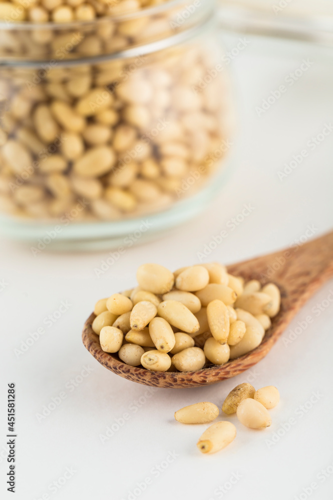 Peeled pine nuts on a wooden spoon and in a glass jar on a light background. Peeled pine nuts on a wooden spoon and in a glass jar on a light background.