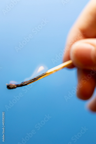Ein brennendes Streichholz wird von Fingern gehalten vor blauem Hintergrund