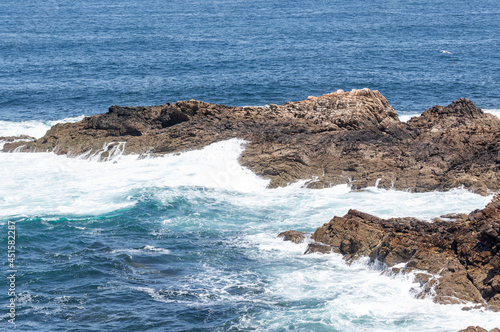 Waves hitting lonely rocks in the sea, contrasting with its intense blue colour, close up.