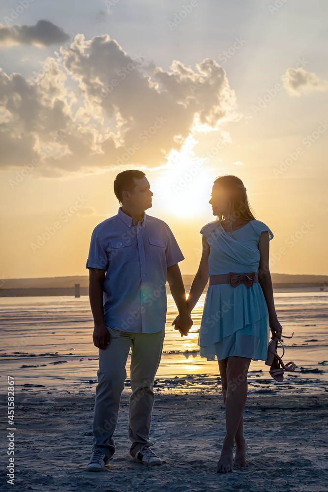Happy relationship concept, family travel option. Vertical photography, full-length people. A loving couple a man and a young woman at sunset hold a hand