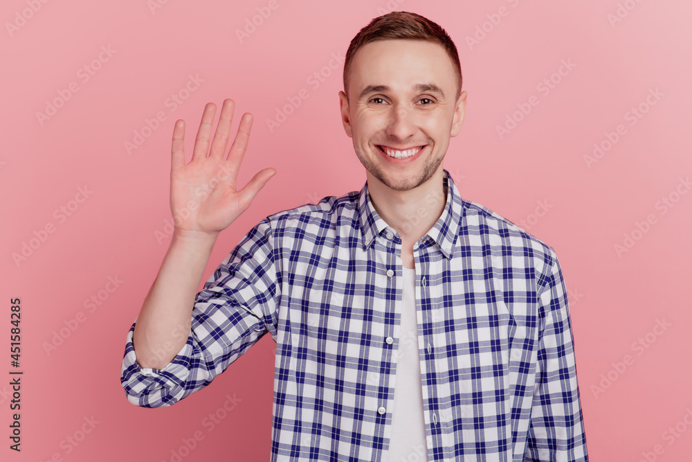 Fototapeta premium Friendly smiling man waving hand to greet you make hi gesture and looking happy to see you standing over pink background