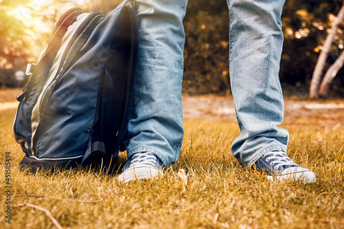 Young teenager foot and legs with sneakers, jeans and a backpack on autumn garden grass. Back to school
