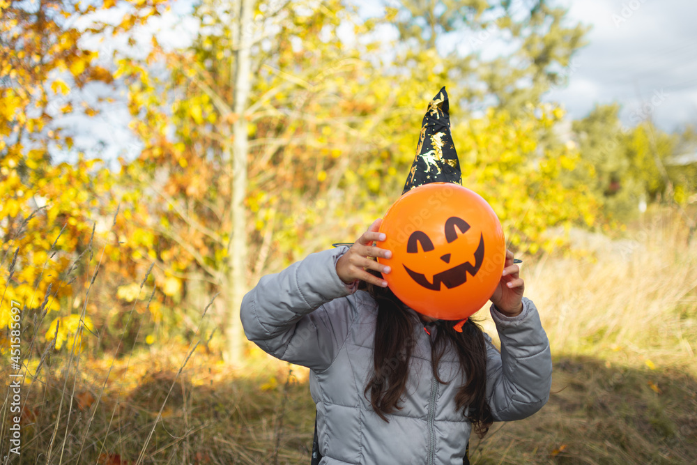 Obraz premium Halloween kids. Little girl with jack o' lantern in witch hat with pumpkin. Toddler kid in witch costume playing in autumn park.