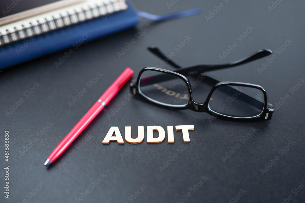 AUDIT letterings on the black background with a pen, eyeglasses, and notebook AUDIT letterings on the black background with a pen, eyeglasses, and notebook