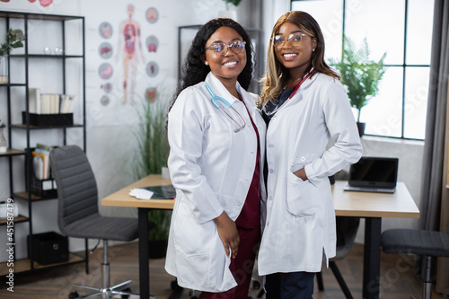 Portrait of two female African American doctors or nurses colleagues  smiling to camera while posing indoors in modern hospital office