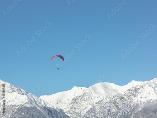 the red wing of the paraglider against the background of the blue sky and the snow-white peaks of the high mountains. the parachutist during the flight against the background of the Alpine mountains