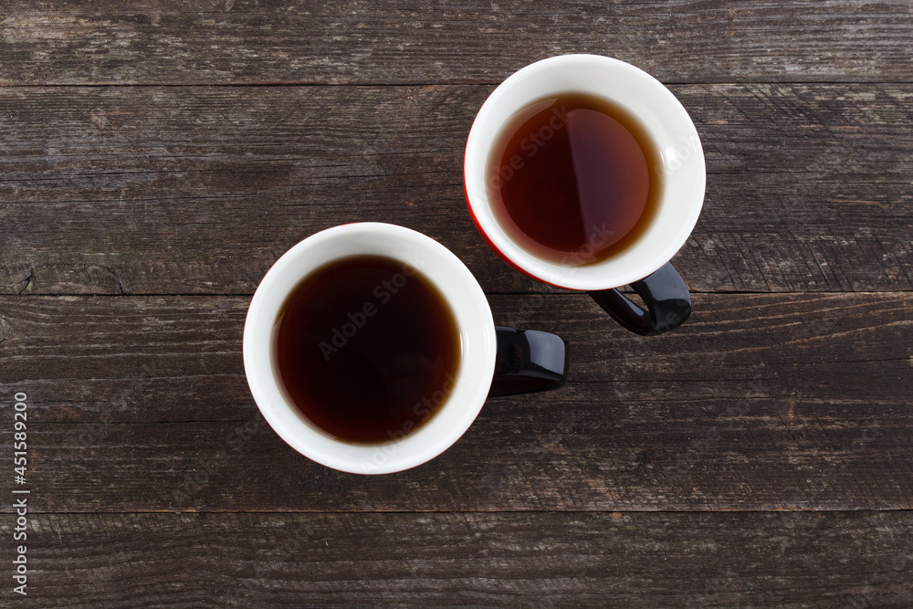A pair of cups with black tea on the background of a table made of wooden boards. A pair of cups with black tea on the background of a table made of wooden boards.