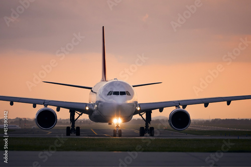 Wide-body airplane taxiing for take off. Front view of plane against airport at sunset..