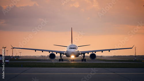 Wide-body airplane taxiing for take off. Front view of plane against airport at sunset..