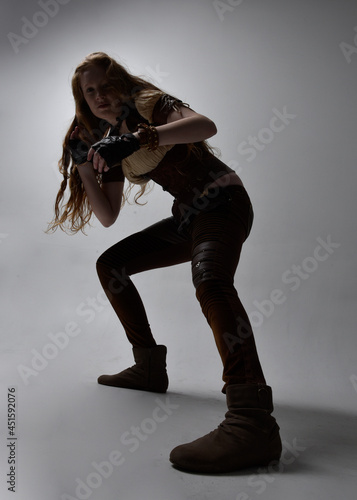 Full length portrait of beautiful young woman with long red hair, wearing steampunk inspired costume. Standing action pose isolated on studio background.