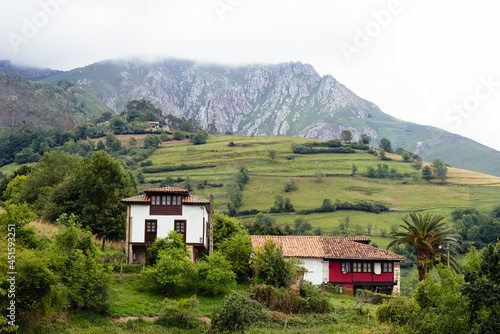 Scenic view of valley in Asturias with traditional farm buildings and green meadows a foggy day. La Goleta, Pilona, Spain