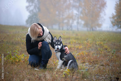 Young woman with beautiful siberian husky dog playing in city park during autumn photo