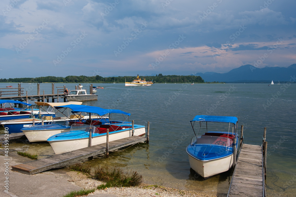 Am Ufer vom Chiemsee in Bayern: Kleine Boote und ein Ausflugsschiff im Hintergrund - dahinter die Berge der Aplen
