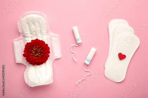 Menstrual tampons and pads on pink background. Menstruation cycle. Hygiene and protection. A rose flower lies on a menstrual pad. photo