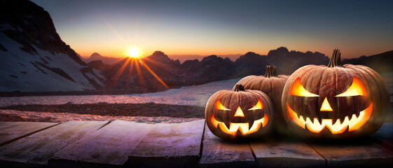 A mountain sunset with the spooky evil glowing eyes of Jack O' Lanterns on the right of a wooden bench on halloween night.