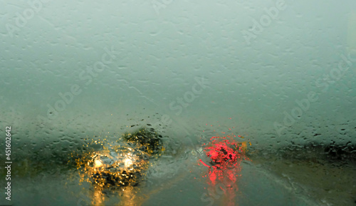 Fototapeta Naklejka Na Ścianę i Meble -  Defocussed traffic viewed through a car windscreen covered in rain,. Focus on raindrops. This is in the fall