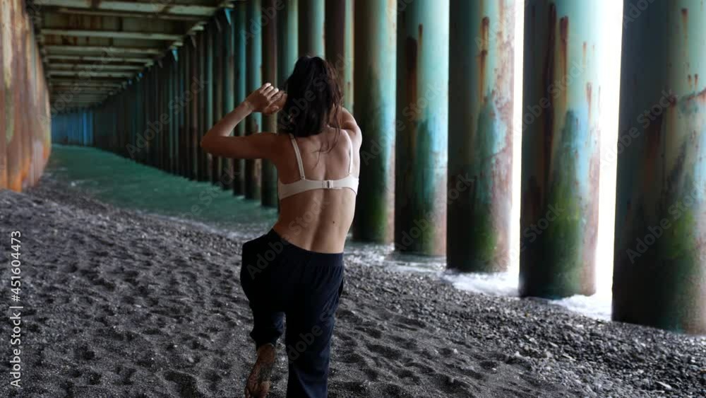 energy woman is dancing under pier on sea coast, wriggling her sexy body and swaying by dark hair energy woman is dancing under pier on sea coast, wriggling her sexy body and swaying by dark hair