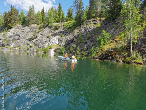 View of the rocky shores and turquoise waters of the Marble Canyon, where boat with tourists float, in the Ruskeala Mountain Park on a sunny summer day.