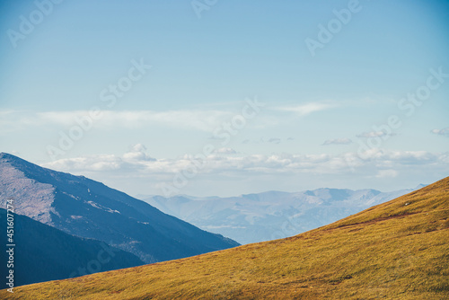Minimalist autumn landscape with diagonal of sunlit orange mountainside on background of mountains silhouettes on horizon. Minimal mountain scenery with slope of hill in golden sunlight in autumn time