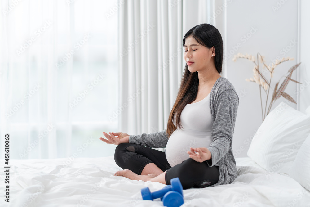 Asian happy pregnant woman is sitting and exercise on the bed. pregnancy, motherhood, people and expectation concept Asian happy pregnant woman is sitting and exercise on the bed. pregnancy, motherhood, people and expectation concept