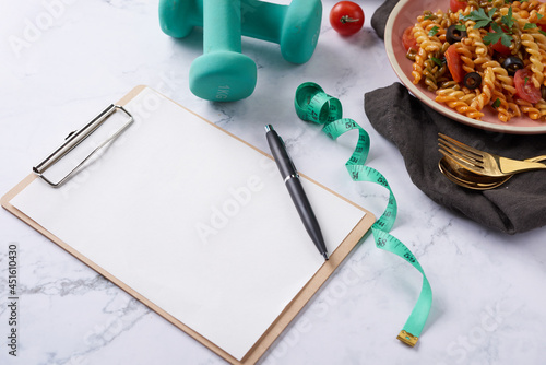 Diet plan, menu or program, tape measure, water, dumbbells and diet food, top view. Vegetarian vegetable pasta. Tasty appetizing classic italian spaghetti pasta with tomato sauce. salad. clipboard photo