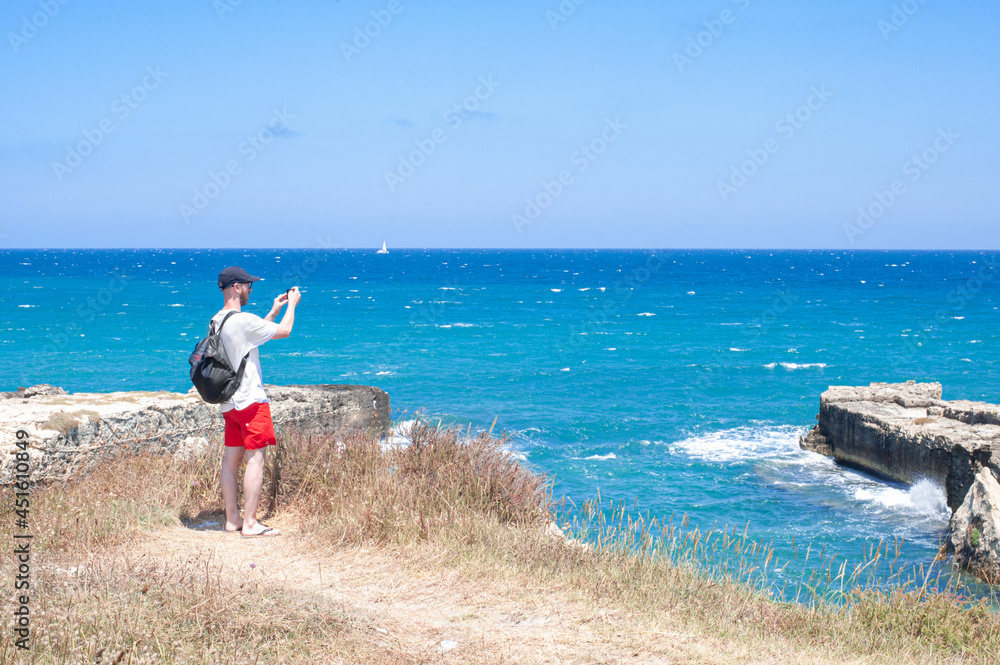 torist man by the sea taking pickture of tha adriatic sea with his phone by Grotta della Poesia
