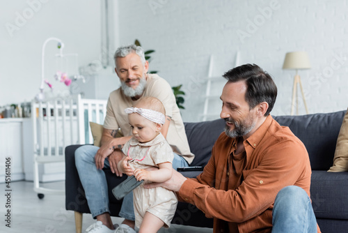 Homosexual father holding toddler kid near smiling partner on blurred background