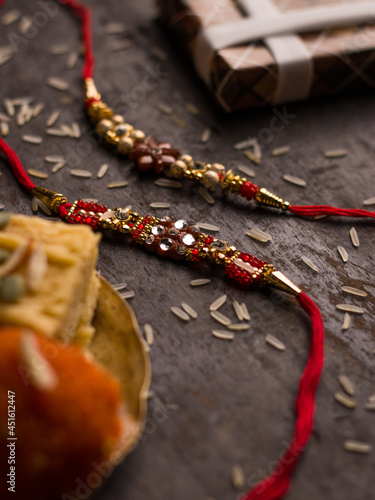 Raksha Bandhan background with an elegant Rakhi and Rice Grains on dark textured background.