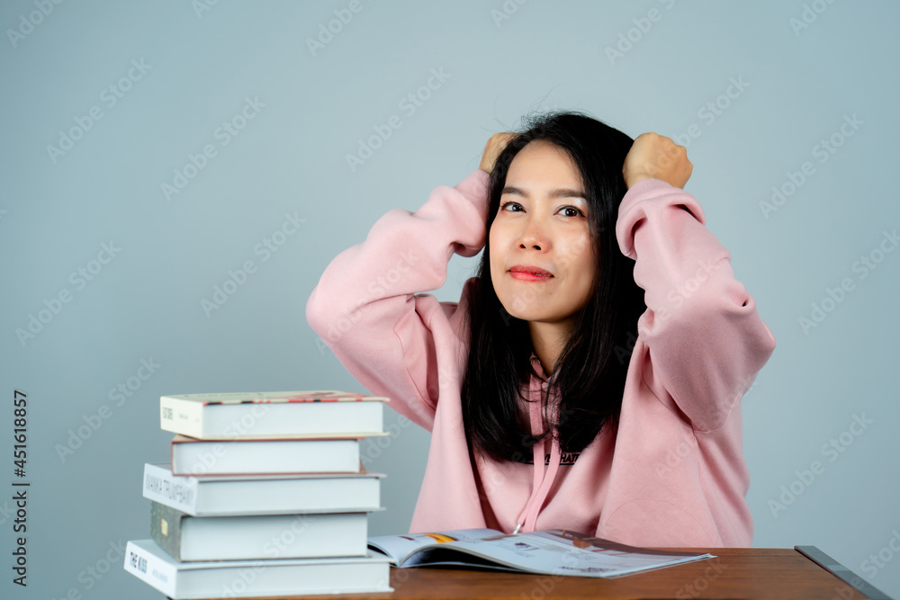 Portrait of an Asian girl wearing a pink shirt. reading a book With a very thoughtful and stressful expression behind the studio gray background. Portrait of an Asian girl wearing a pink shirt. reading a book With a very thoughtful and stressful expression behind the studio gray background.