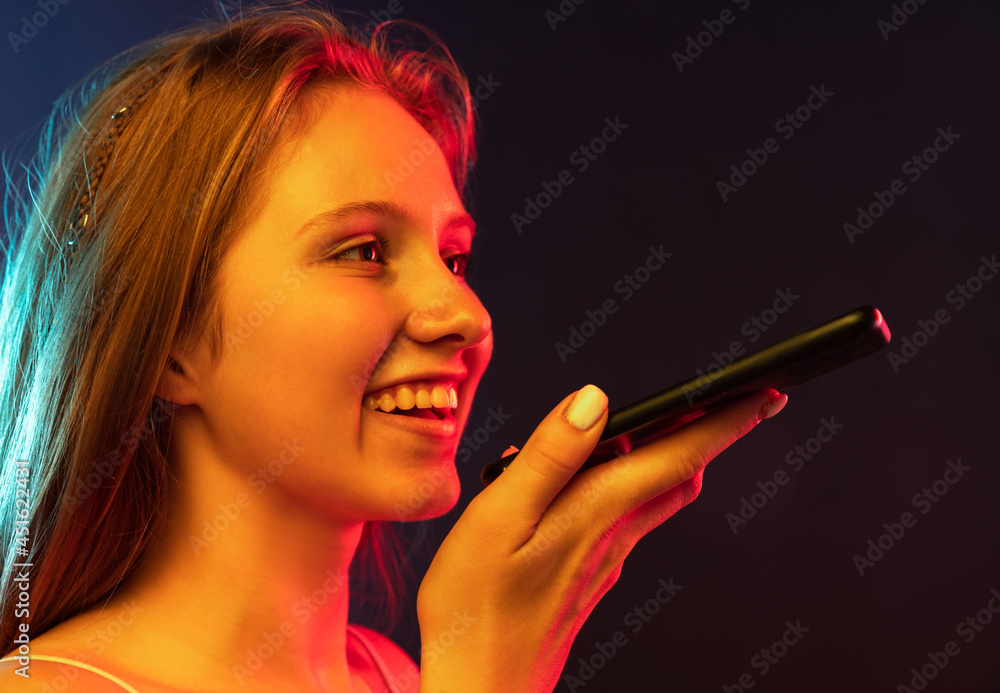 Obraz premium Close-up young beautiful girl using phone isolated on dark blue studio background. Concept of human emotions, facial expression, youth, sales, ad , gadgets