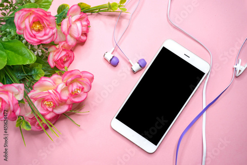 On the table lies a white smartphone on a pink background with flowers