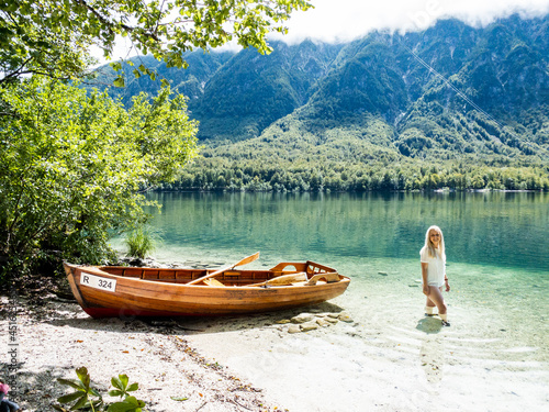 Blonde woman standing in the Bohinj Lake, next to a boat on the beach