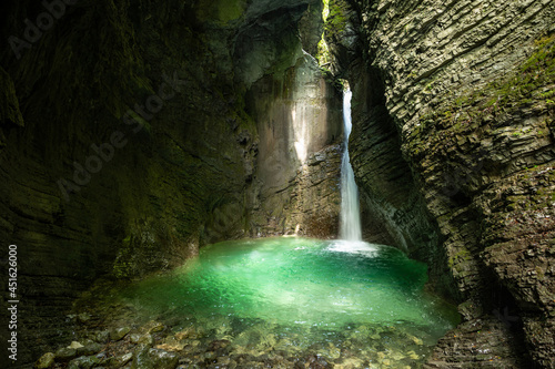 Crystal clear waterfall in a cave flooded with sunlight and blue water