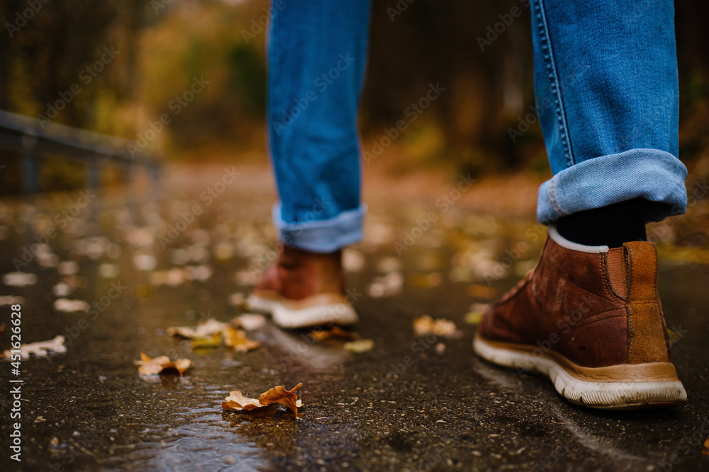 feet of a woman walking along asphalt road in autumn forest in the rain. Pair of shoe on slippery road in the fall. Abstract empty blank of the autumn weather