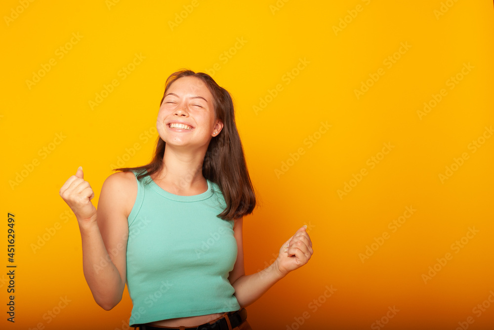 a teenage girl of American appearance on a yellow background in casual clothes with a bright smile on her face in a joyful mood. Emotions of joy, isolates, place for text a teenage girl of American appearance on a yellow background in casual clothes with a bright smile on her face in a joyful mood. Emotions of joy, isolates, place for text