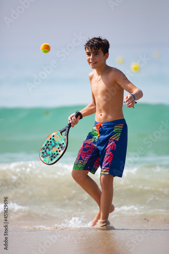 kid playing beach tennis on a sunny day