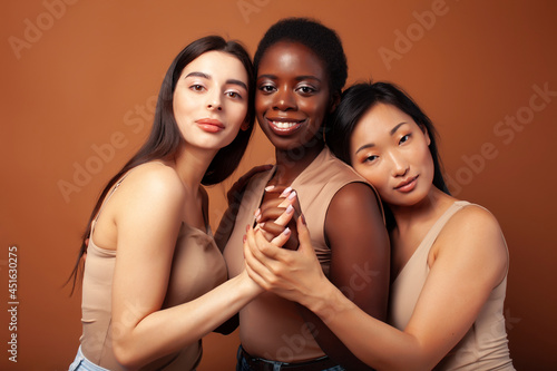young pretty caucasian, afro, scandinavian woman posing cheerful together on brown background, lifestyle diverse nationality people concept