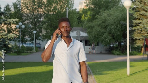 beautiful African American man walks down the street, talking on the phone, in the summer