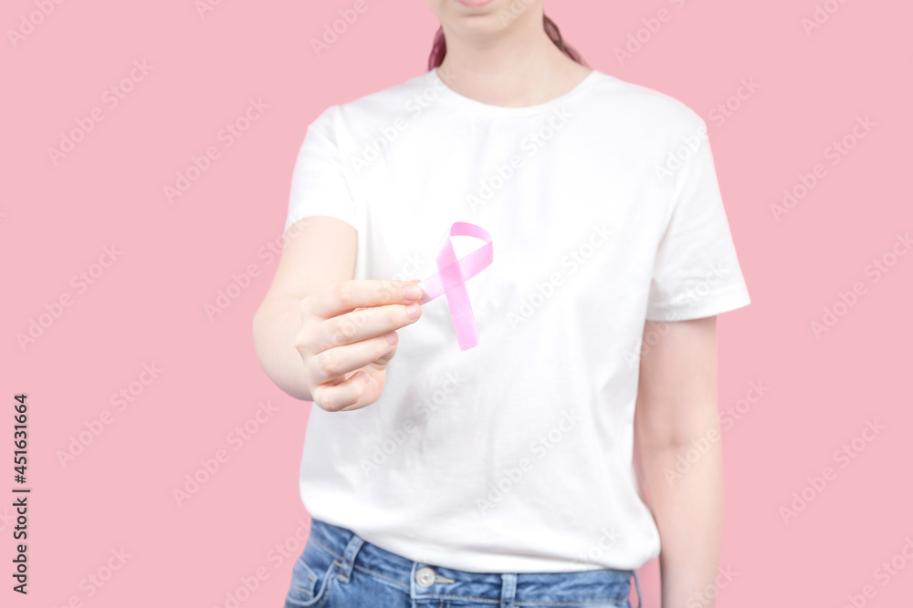 World Breast cancer day concept. Woman in white T-shirt holds pink ribbon in hand. October Breast Cancer Awareness month World Breast cancer day concept. Woman in white T-shirt holds pink ribbon in hand. October Breast Cancer Awareness month